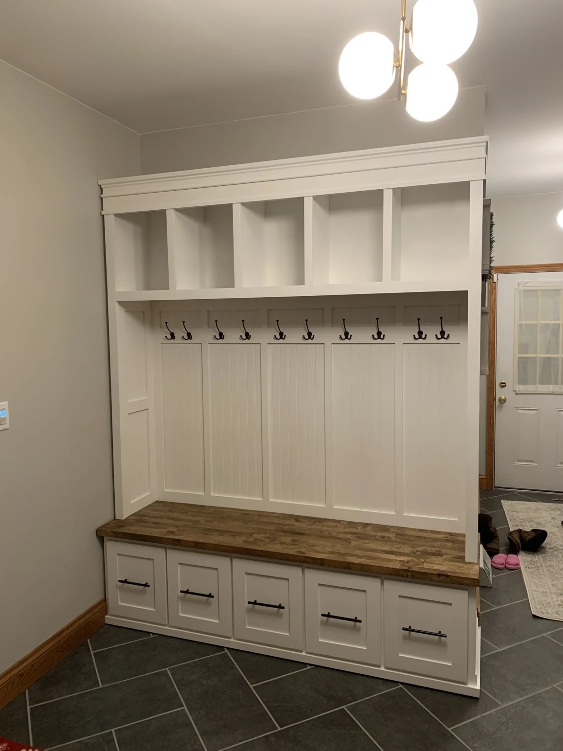 Custom white mudroom built-in with wood bench, drawers, cubbies and coat hooks